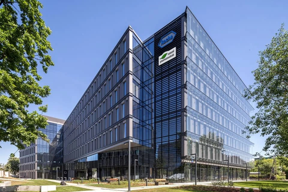 Natural Pharmaceuticals Vistan™  Kaasaegne klaasfassaadiga kontorihoone päikesevalguses, ümbritsetud roheluse ja sinise taevaga.